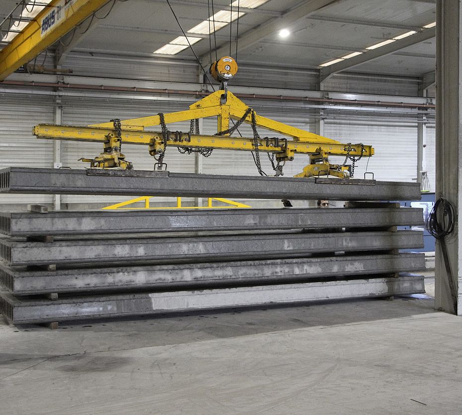Grue ABUS jaune soulevant une dalle préfabriquée en béton dans un hall de production